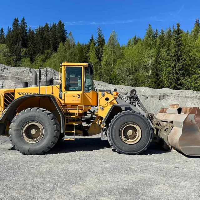 En stor Volvo hjullaster står parkert foran hauger med sand eller pukk i et steinbrudd.