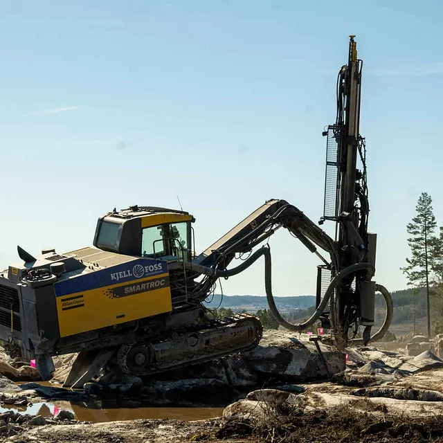 En borerigg står på fjell i et steinbrudd og borer hull for sprenging.