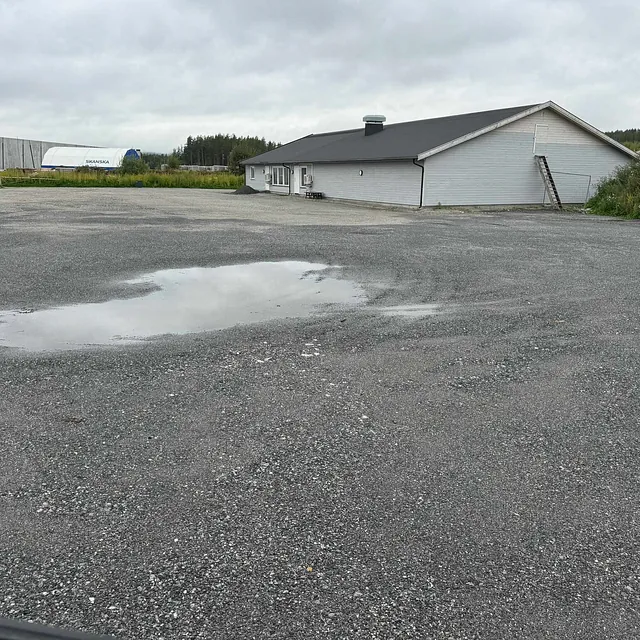 En grusplass med en vanndam foran en lav bygning på et industriområde under en overskyet himmel.