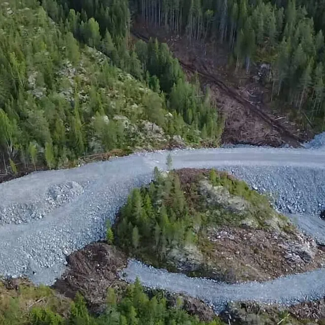 En bred grusvei går over en høyde midt i et skogsområde sett fra luften.
