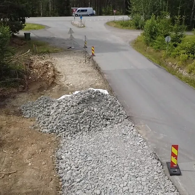 Veiarbeid ved et kryss der en grøft fylles med stein og trafikk kjører forbi.