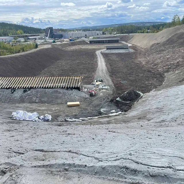 Et stort anleggsområde der terrenget er formet i skråninger med en bygning under oppføring i bunnen.
