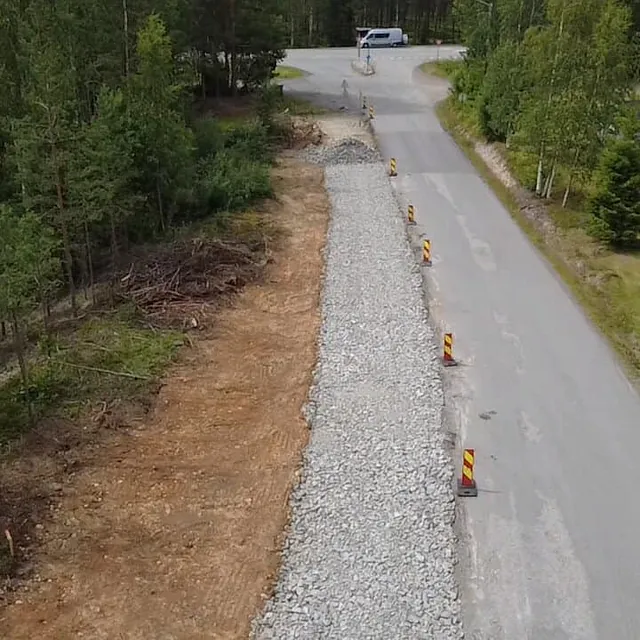 Et veiarbeid langs en skogkledd vei der en grøft fylles med pukk og markeres med trafikkjegler.